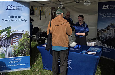 A community member speaks with Residential Tenancies Authority staff at an information booth inside a marquee at NAIDOC Week Family Fun Day 2026.