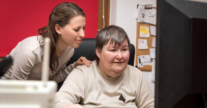 Young person looking at computer screen with support carer.