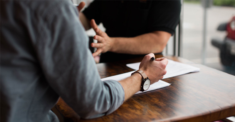 Two people seated at a table, with pen and paper.