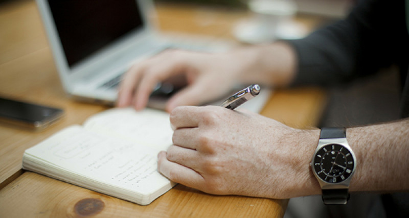 Person typing on a laptop and writing in a notepad