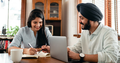 Husband and wife working on documents together at dining table.