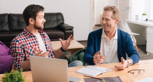 Two men sitting around a laptop having a discussion