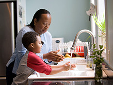 Woman and young boy cleaning hands at kitchen sink