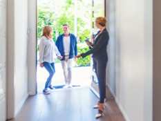 Woman dressed in suit welcoming couple into a vacant house