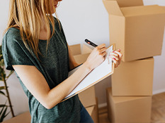 Young woman checking off list with empty cardboard boxes.