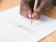 Hand holding pen to sign on paper.