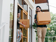 a man and woman carrying large moving boxes out of the house.