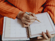 Person in orange jumper writing in a diary calendar with pencil.