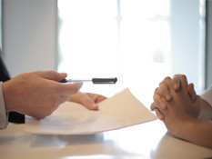 A person handing paper and pen to another person.